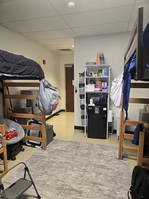 boys dorm room with lofted beds neutral rug and mini kitchen setup with honey can do shelves and over door storage
